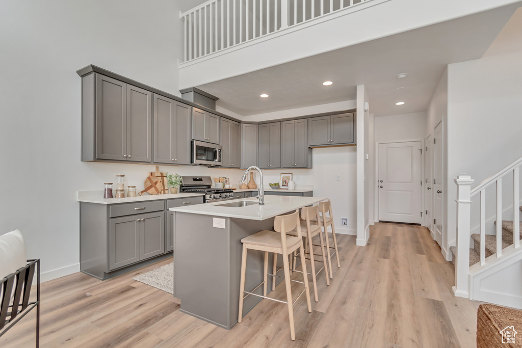 Kitchen featuring a sink, stainless steel appliances, gray cabinets, light wood-style flooring, and a kitchen bar