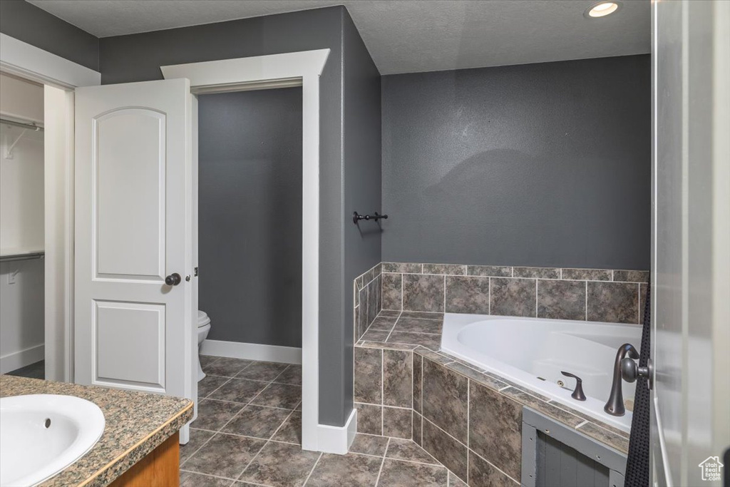 Bathroom featuring a spacious closet, toilet, vanity, tile patterned floors, and a garden tub