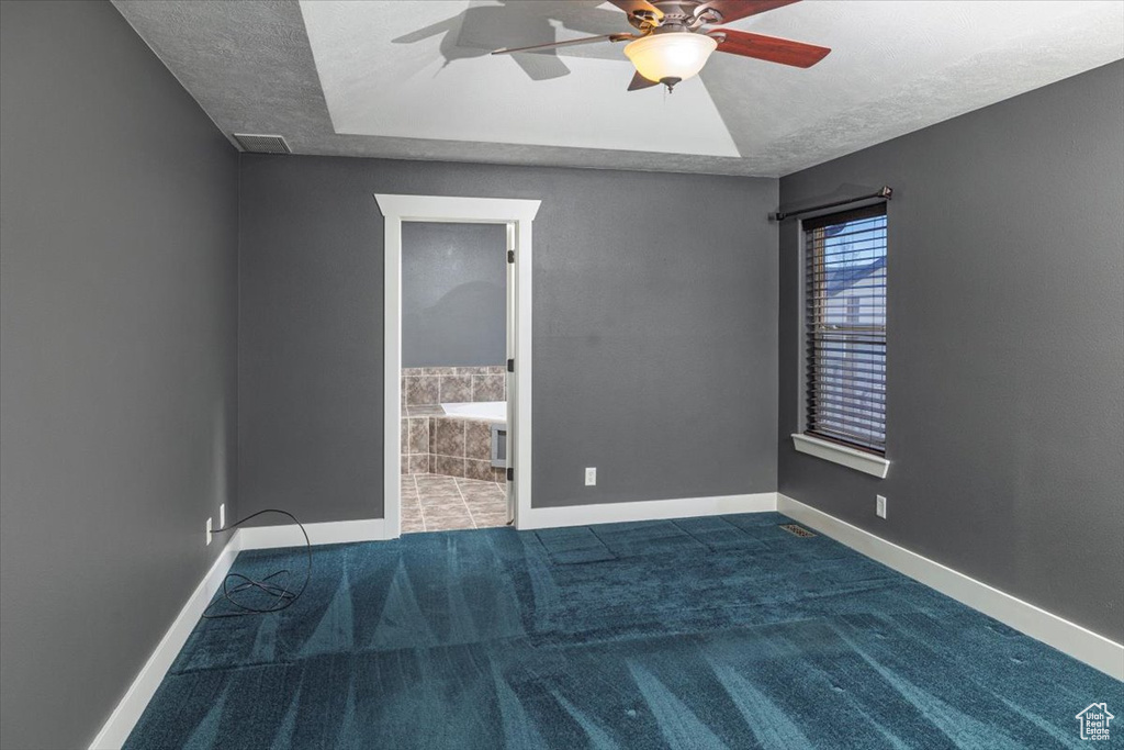 Unfurnished room featuring a raised ceiling, a textured ceiling, ceiling fan, and baseboards