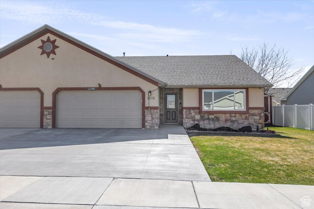 View of front of home with a front yard, stone siding, a garage, concrete driveway, and stucco siding