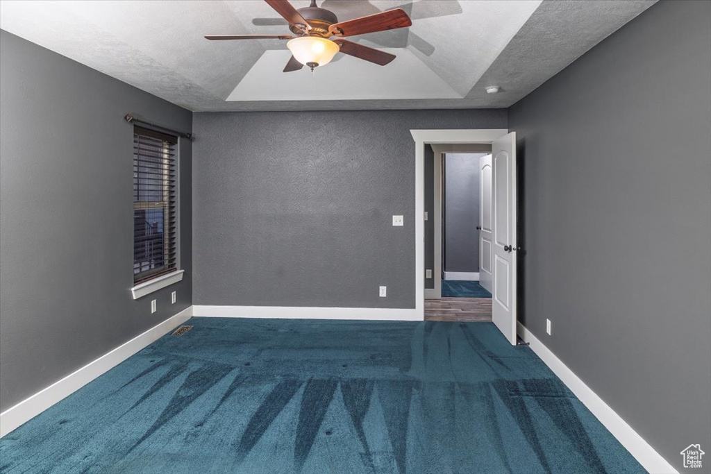 Empty room featuring carpet, baseboards, a ceiling fan, and a raised ceiling