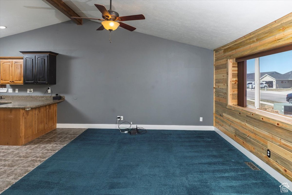 Interior space featuring ceiling fan, visible vents, vaulted ceiling with beams, wooden walls, and baseboards