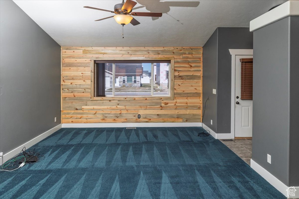 Carpeted empty room with wooden walls, baseboards, a ceiling fan, and an accent wall