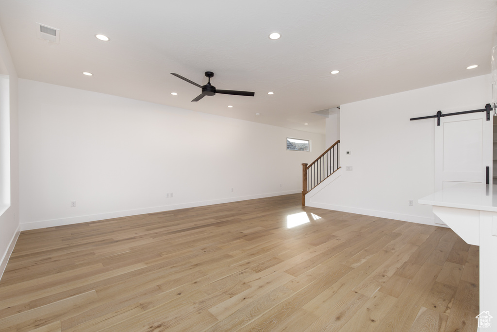 Unfurnished living room featuring stairway, a ceiling fan, a barn door, light wood-style floors, and visible vents