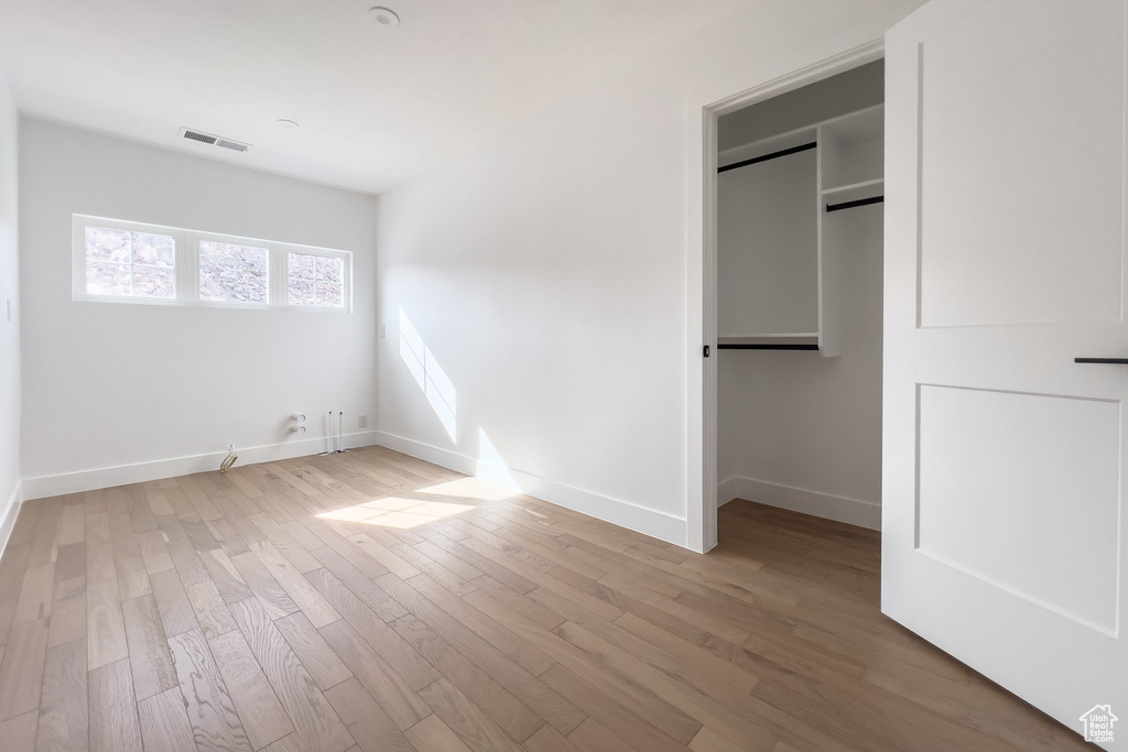 Unfurnished bedroom with a spacious closet, visible vents, baseboards, and light wood-type flooring