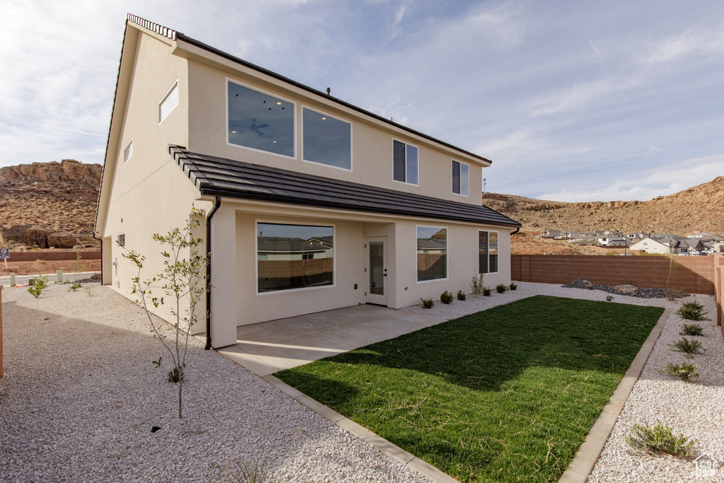 Rear view of property featuring a mountain view, a patio area, a yard, fence, and stucco siding