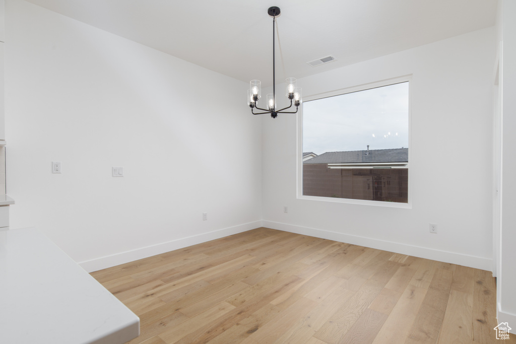 Unfurnished dining area featuring visible vents, baseboards, a notable chandelier, and light wood-style floors