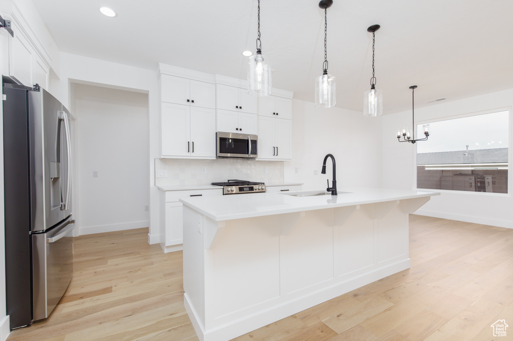 Kitchen featuring tasteful backsplash, light countertops, appliances with stainless steel finishes, light wood finished floors, and a sink