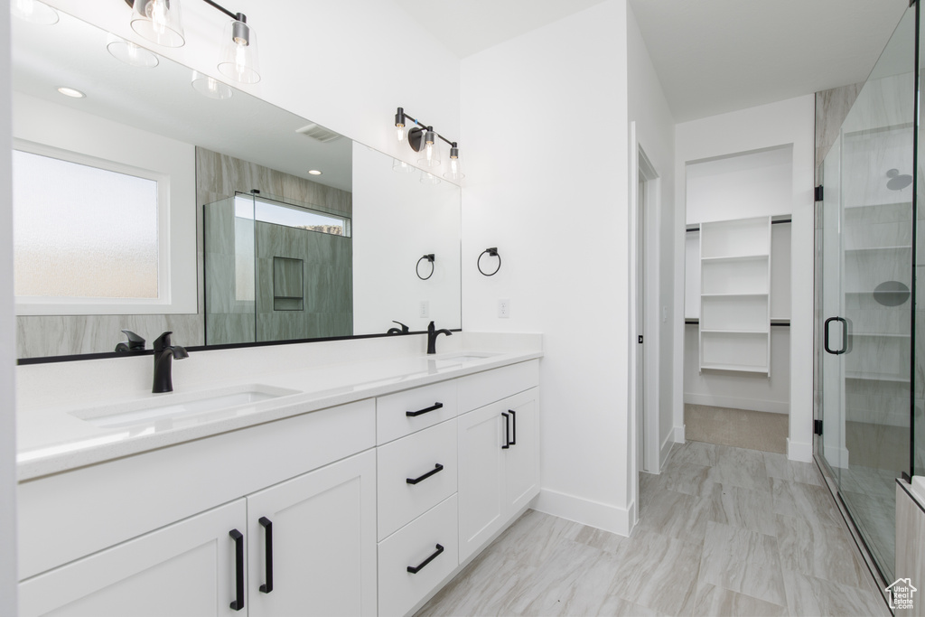 Bathroom featuring a shower stall, double vanity, a spacious closet, and a sink