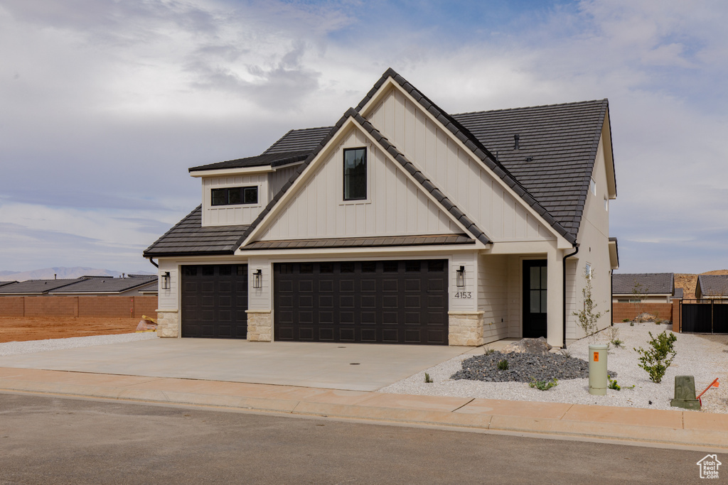 Modern farmhouse featuring an attached garage, stone siding, board and batten siding, fence, and driveway