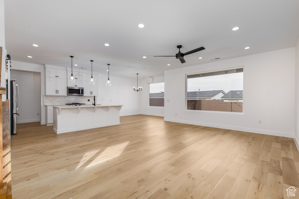 Unfurnished living room with recessed lighting, light wood finished floors, ceiling fan with notable chandelier, and baseboards