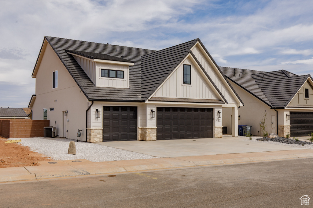 Modern inspired farmhouse with central AC, an attached garage, stone siding, board and batten siding, and driveway