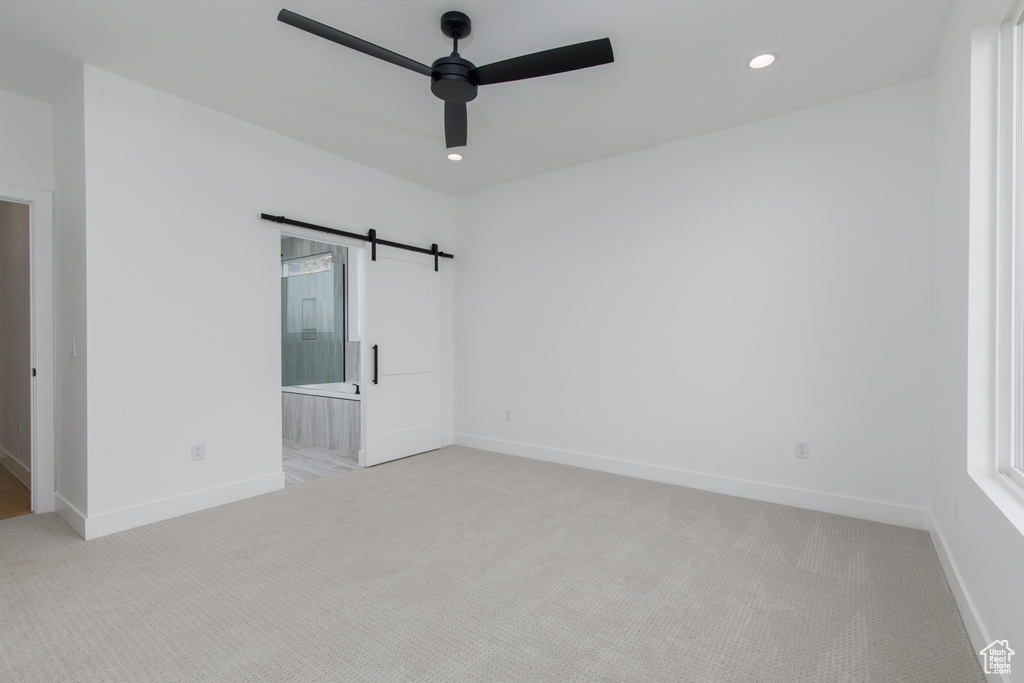 Empty room with baseboards, a ceiling fan, light colored carpet, and a barn door