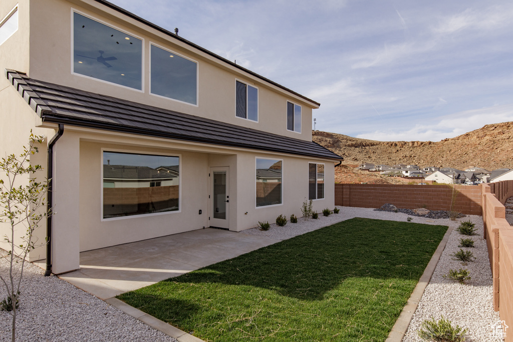 Rear view of house featuring a fenced backyard, stucco siding, a lawn, a patio, and a mountain view