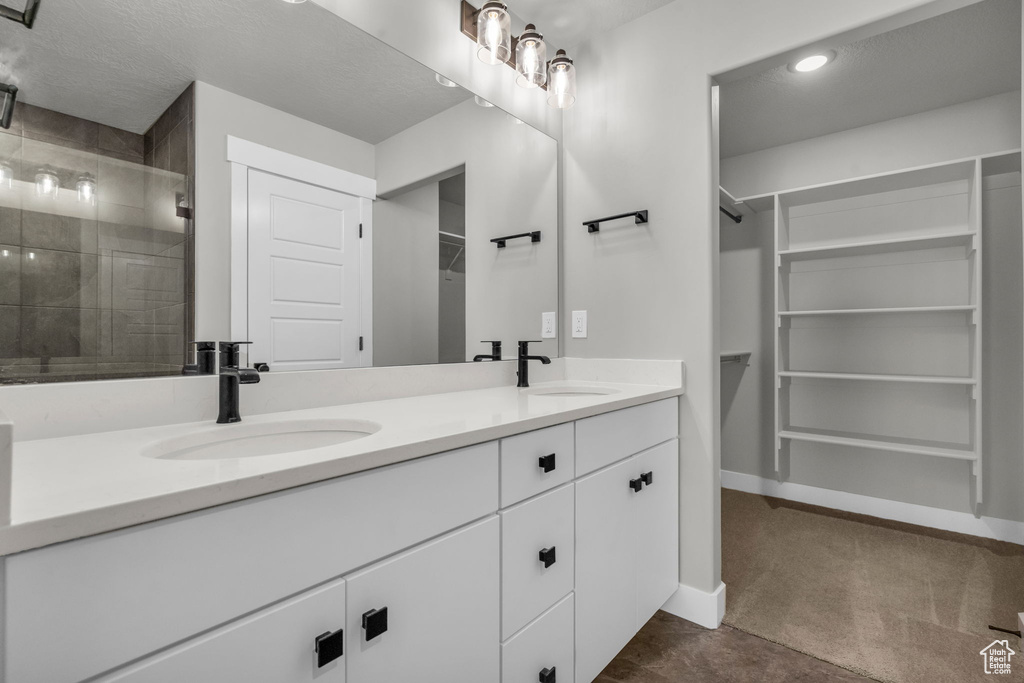Full bath with a stall shower, double vanity, a sink, and a spacious closet