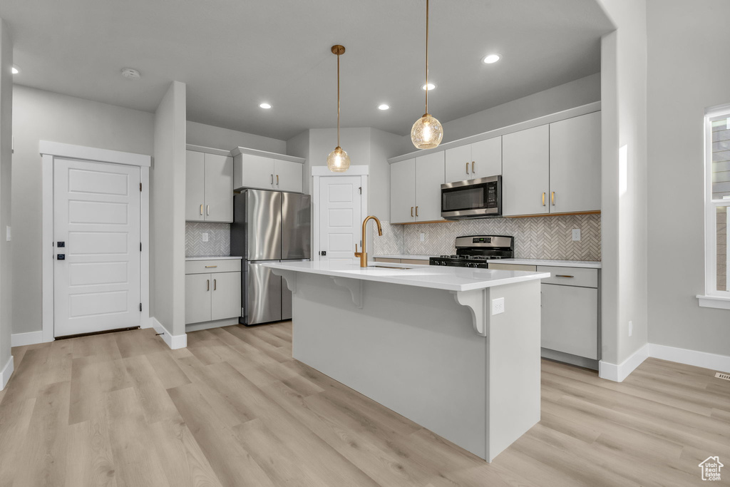 Kitchen featuring a kitchen breakfast bar, light countertops, stainless steel appliances, light wood finished floors, and a sink