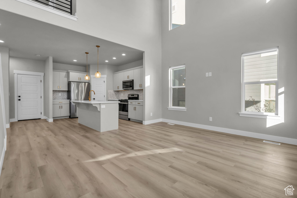Kitchen featuring an island with sink, light wood-type flooring, appliances with stainless steel finishes, open floor plan, and baseboards