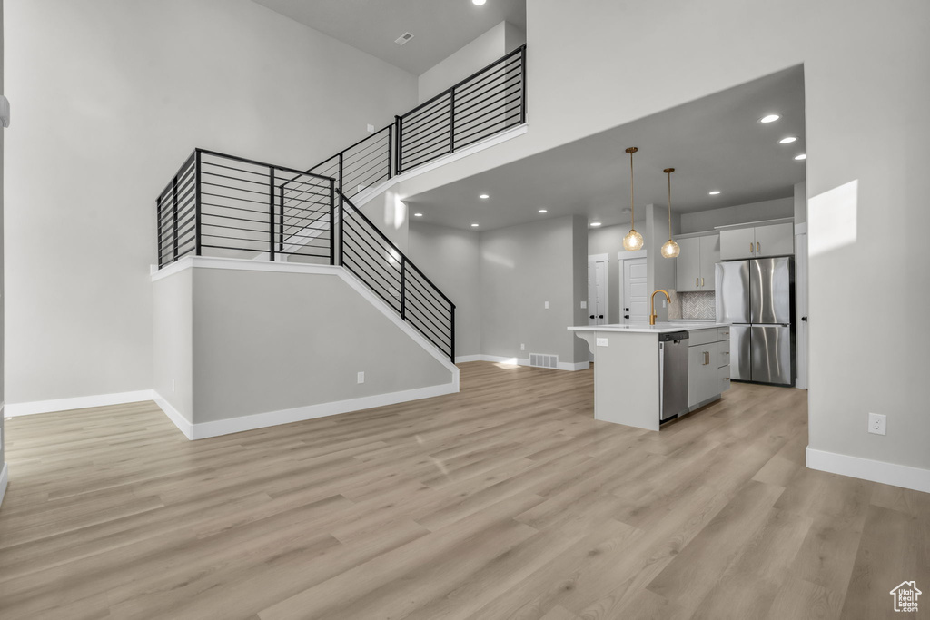 Unfurnished living room featuring stairs, light wood finished floors, baseboards, and a sink