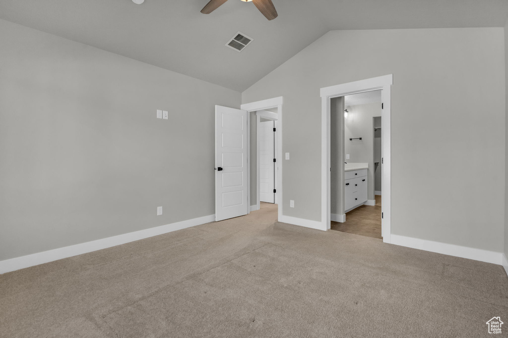 Unfurnished bedroom with connected bathroom, light colored carpet, visible vents, lofted ceiling, and baseboards