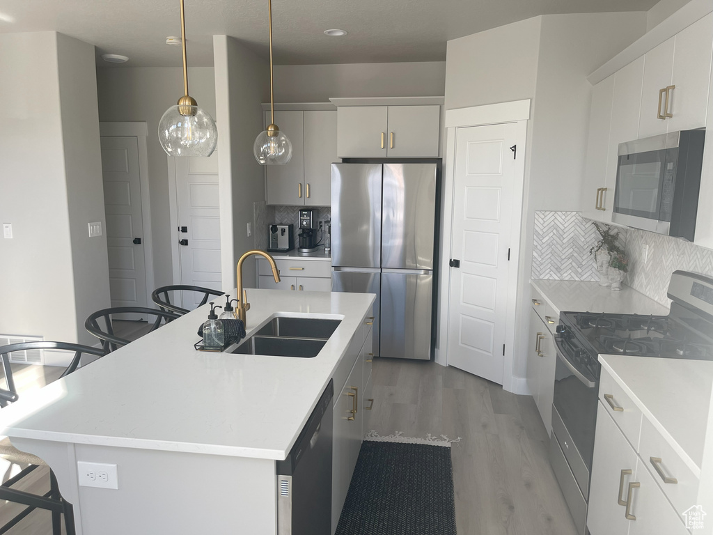 Kitchen featuring light wood-style floors, appliances with stainless steel finishes, a sink, a center island with sink, and a breakfast bar area