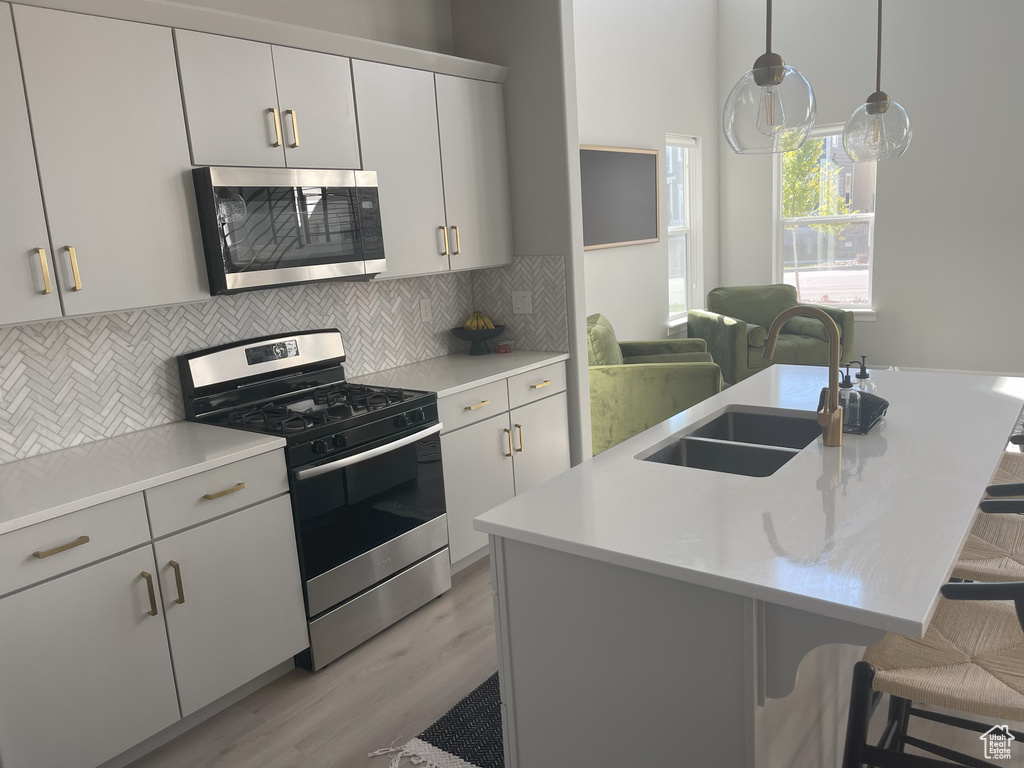 Kitchen featuring a sink, appliances with stainless steel finishes, a breakfast bar, backsplash, and light wood-style flooring