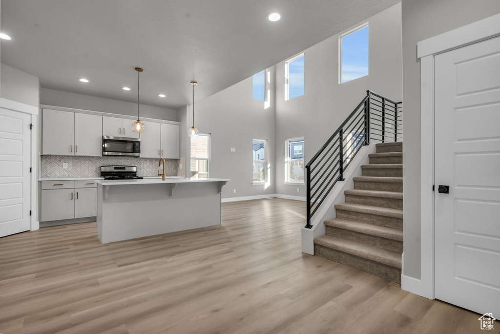Kitchen with light countertops, a kitchen island with sink, stainless steel appliances, light wood-style flooring, and decorative backsplash
