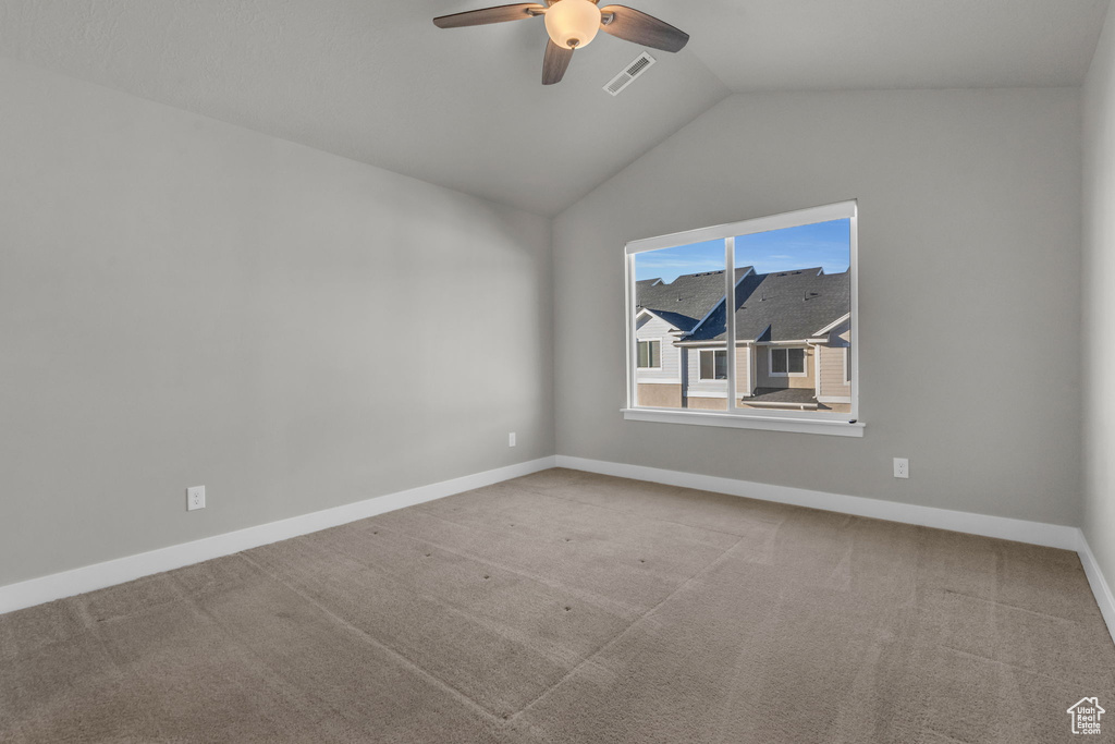 Carpeted empty room with visible vents, baseboards, a ceiling fan, and vaulted ceiling
