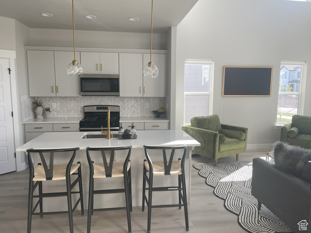 Kitchen with light wood finished floors, decorative light fixtures, light countertops, and appliances with stainless steel finishes