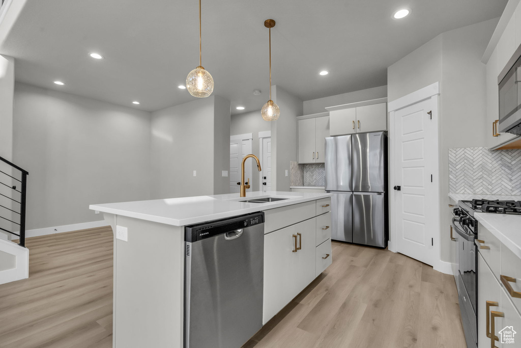 Kitchen featuring a sink, light countertops, appliances with stainless steel finishes, an island with sink, and light wood-style floors