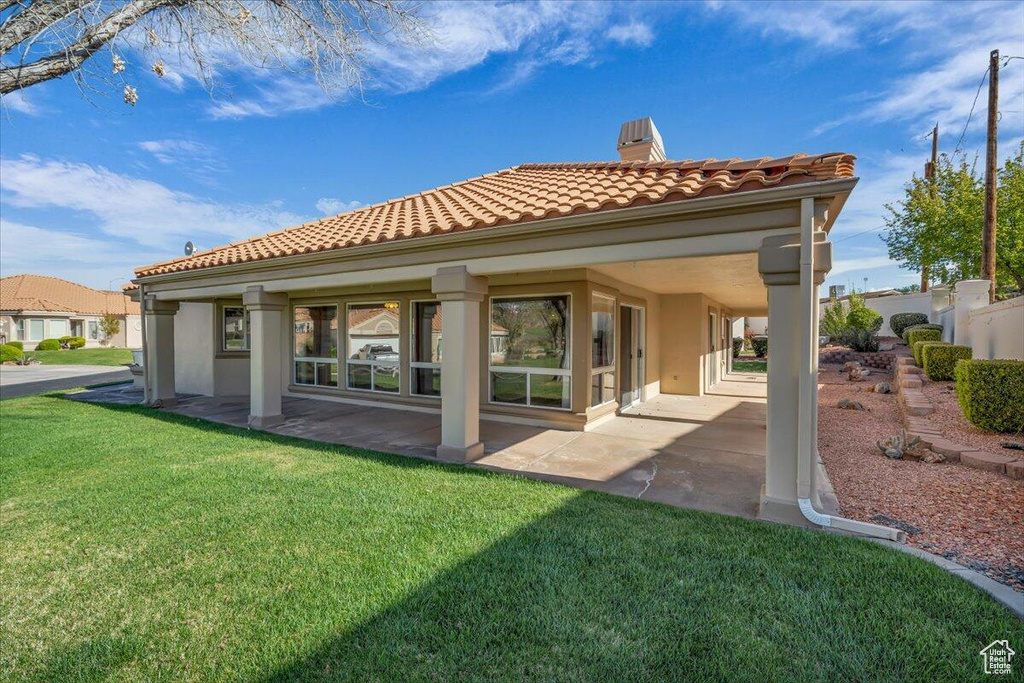 Back of property with a lawn, a chimney, a tile roof, a patio, and stucco siding