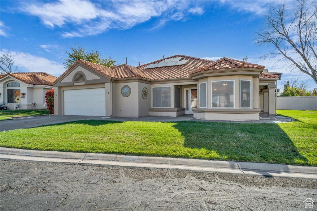 Mediterranean / spanish-style home featuring a front lawn, solar panels, a tile roof, a garage, and driveway