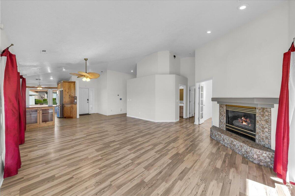 Living room featuring high vaulted ceiling, ceiling fan, a fireplace, light wood-style flooring, and recessed lighting