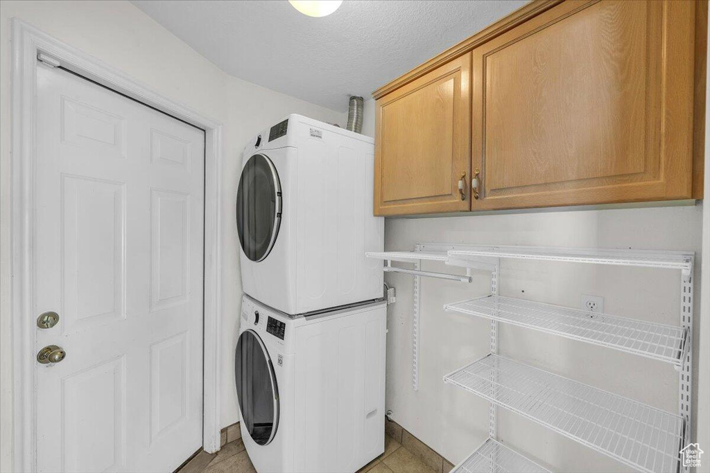 Washroom with a textured ceiling, stacked washer and dryer, light tile patterned floors, and cabinet space