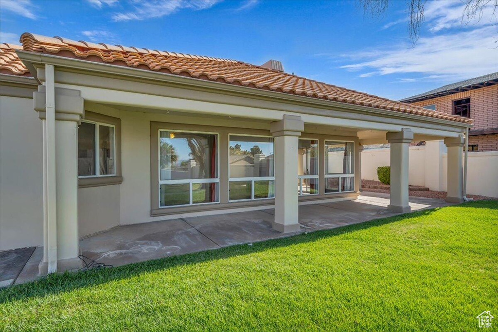 Back of house featuring a patio area, a tiled roof, a lawn, fence, and stucco siding
