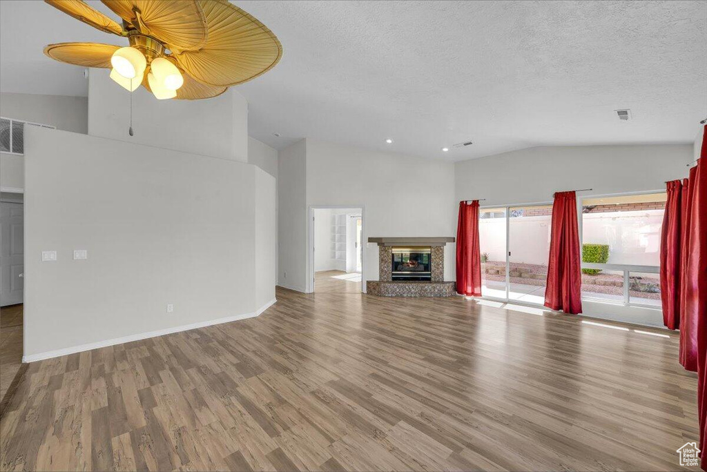 Unfurnished living room with ceiling fan, a textured ceiling, wood finished floors, lofted ceiling, and a premium fireplace