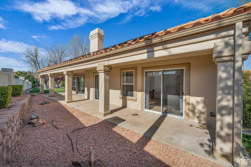 Back of house featuring a tiled roof, a chimney, fence, a patio, and stucco siding