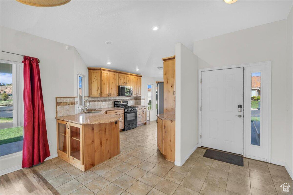 Kitchen featuring light stone countertops, gas stove, a sink, stainless steel microwave, and backsplash