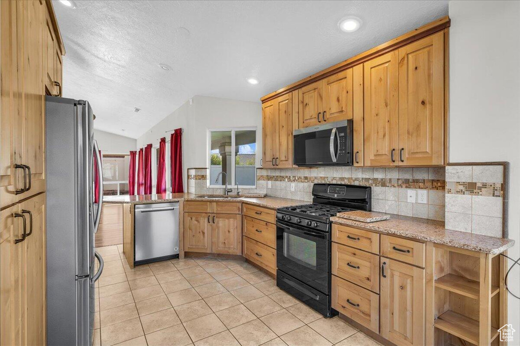 Kitchen featuring vaulted ceiling, light stone counters, light tile patterned flooring, appliances with stainless steel finishes, and a sink