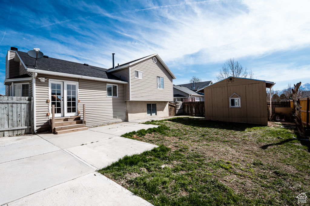 Rear view of house featuring entry steps, a patio area, a shingled roof, and an outbuilding