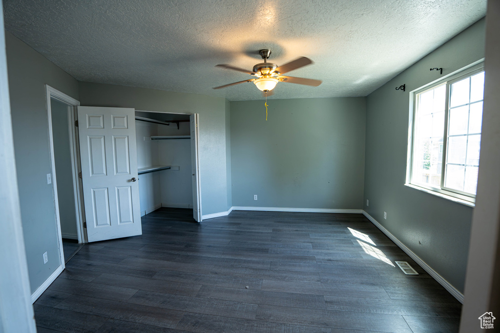 Unfurnished bedroom with a textured ceiling, dark wood finished floors, a closet, a ceiling fan, and baseboards