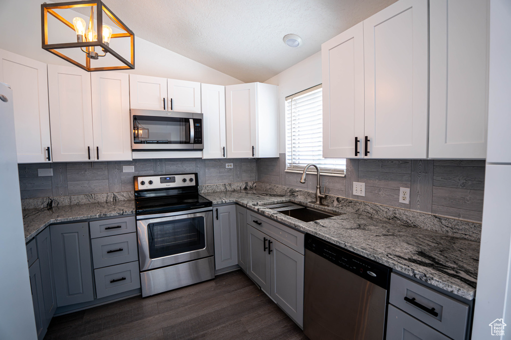 Kitchen with stainless steel appliances, a sink, vaulted ceiling, decorative backsplash, and light stone counters