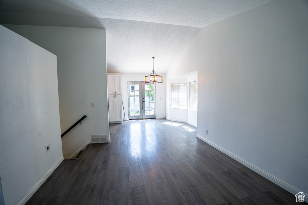 Unfurnished living room featuring dark wood-style flooring, a chandelier, baseboards, vaulted ceiling, and a textured ceiling