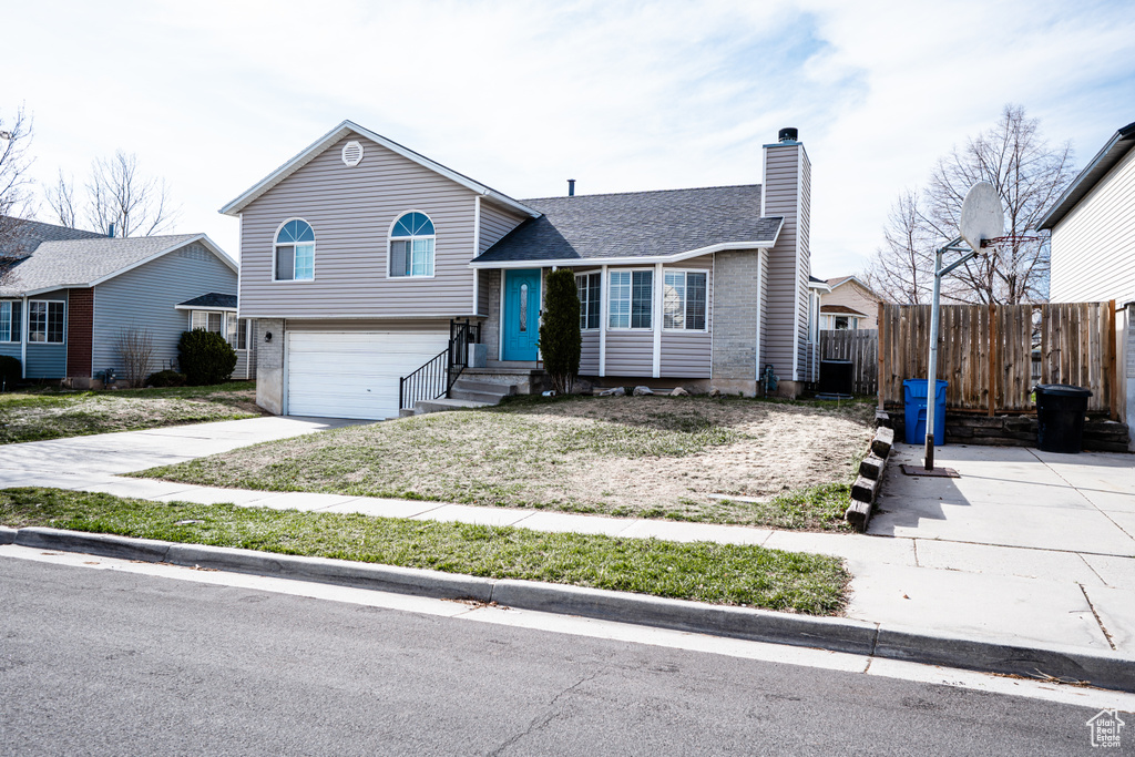 Split level home featuring a chimney, a garage, driveway, brick siding, and roof with shingles
