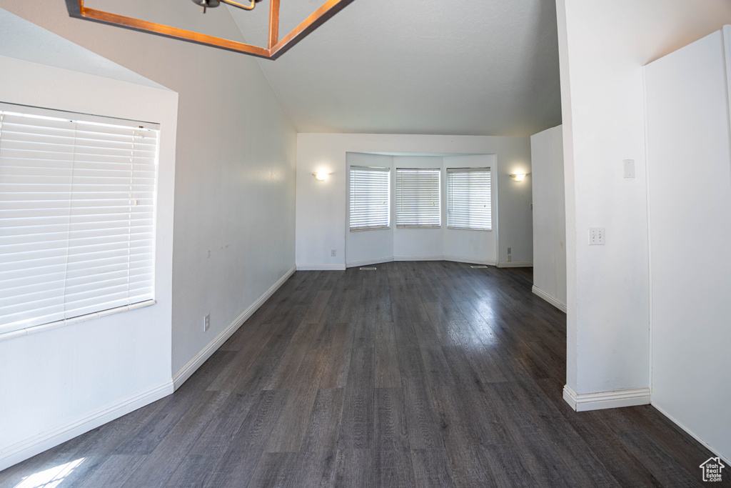 Spare room featuring dark wood-style flooring, lofted ceiling, and baseboards
