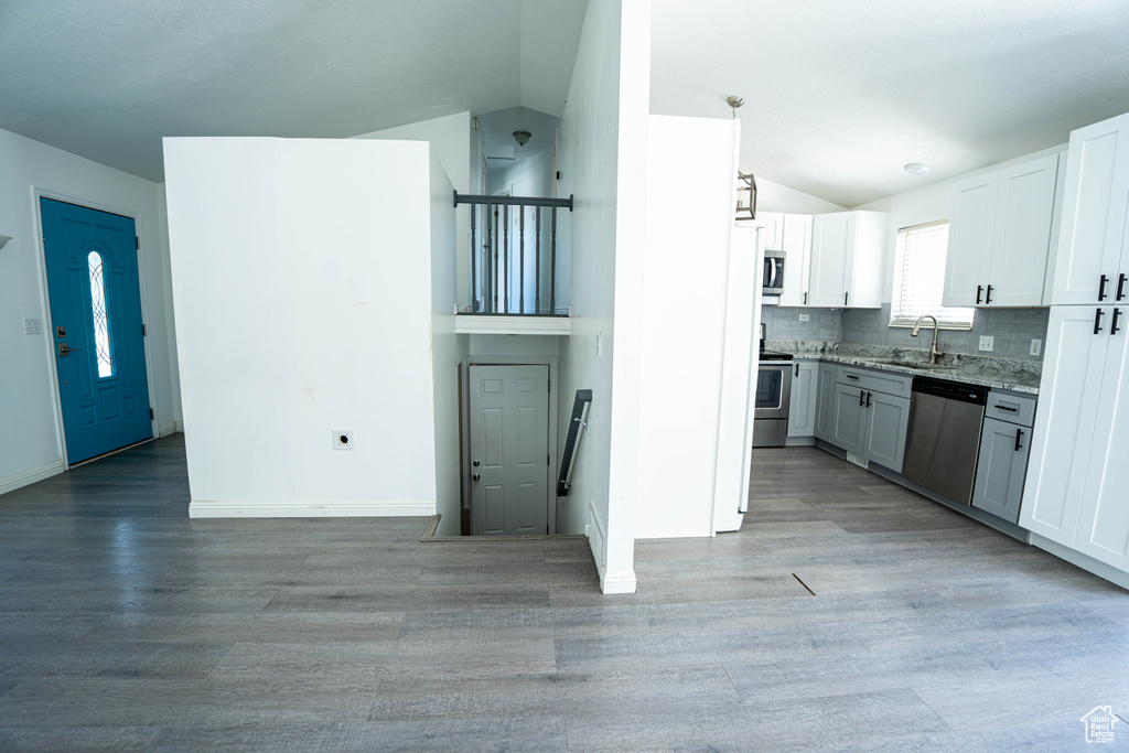 Kitchen featuring appliances with stainless steel finishes, lofted ceiling, a sink, light wood-style floors, and light stone countertops