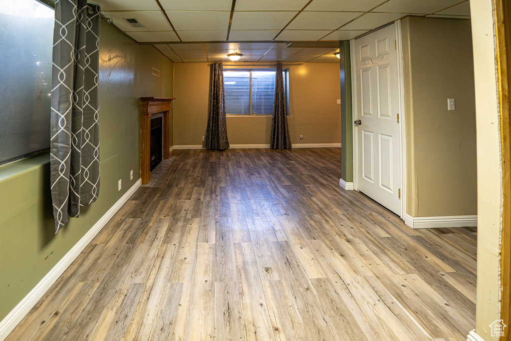 Unfurnished living room featuring a paneled ceiling, a fireplace, wood finished floors, and baseboards