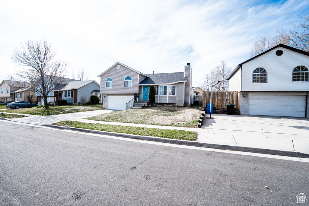 Split level home with an attached garage, driveway, a chimney, and entry steps