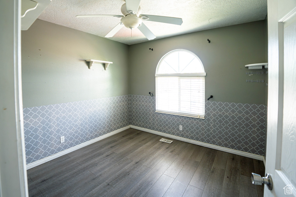 Unfurnished room featuring a wainscoted wall, a ceiling fan, dark wood-style floors, baseboards, and a textured ceiling