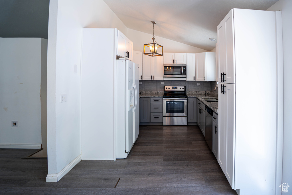 Kitchen with appliances with stainless steel finishes, vaulted ceiling, dark wood-style flooring, backsplash, and a chandelier