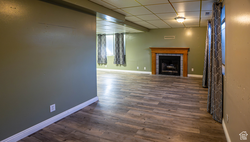Unfurnished living room with a tile fireplace, wood finished floors, a drop ceiling, and baseboards